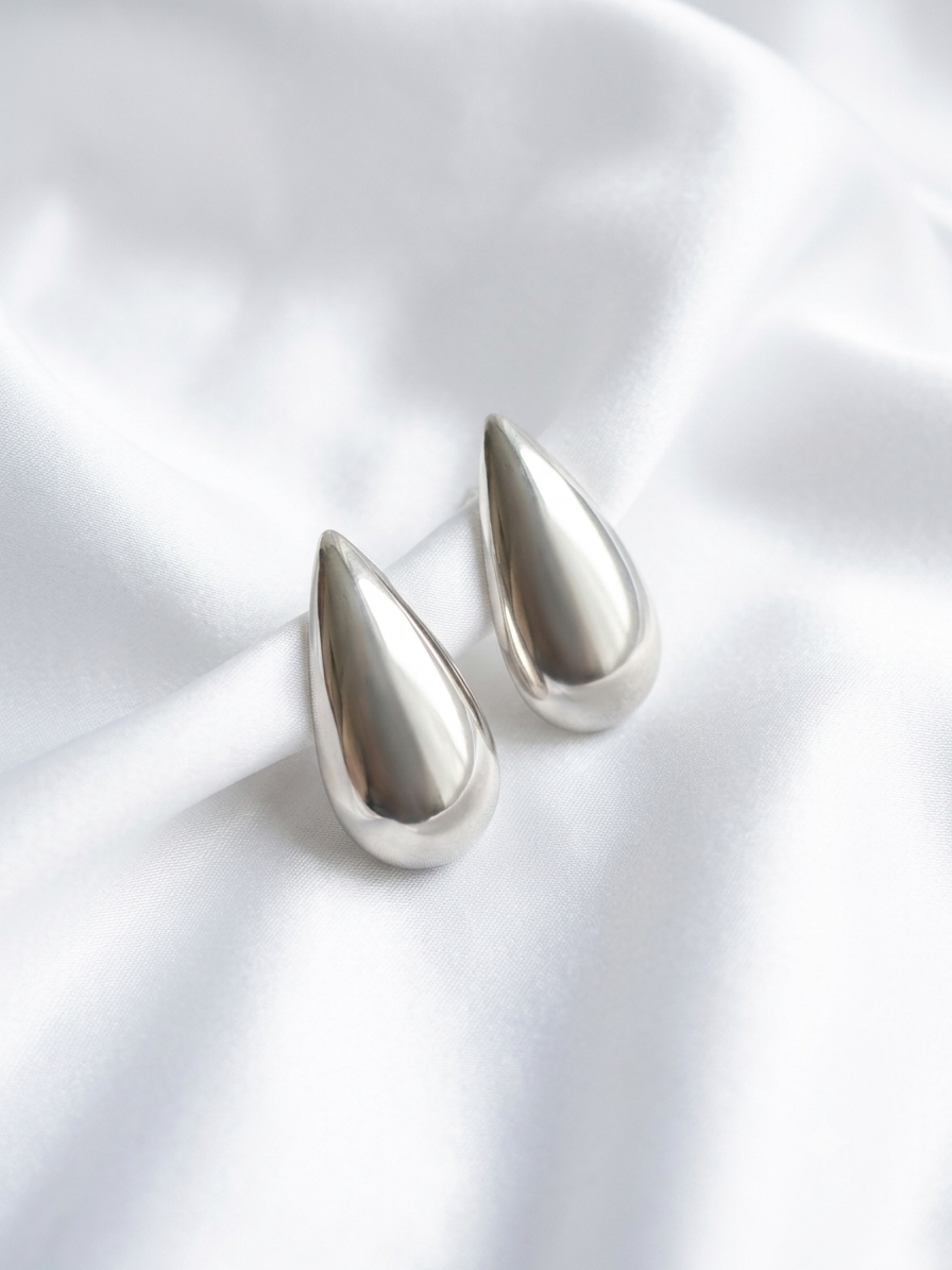Brincos de gota prateados em design fluido e anatômico. Peça moderna com acabamento espelhado de alto brilho, perfeita para destacar produções sofisticadas ou elevar o visual do dia a dia.